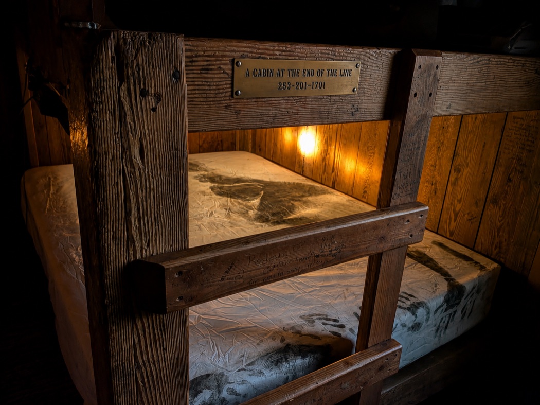cabin 8 bunks with body-print sheets and a carved brass sign reading a cabin at the end of the line, 253-201-1701