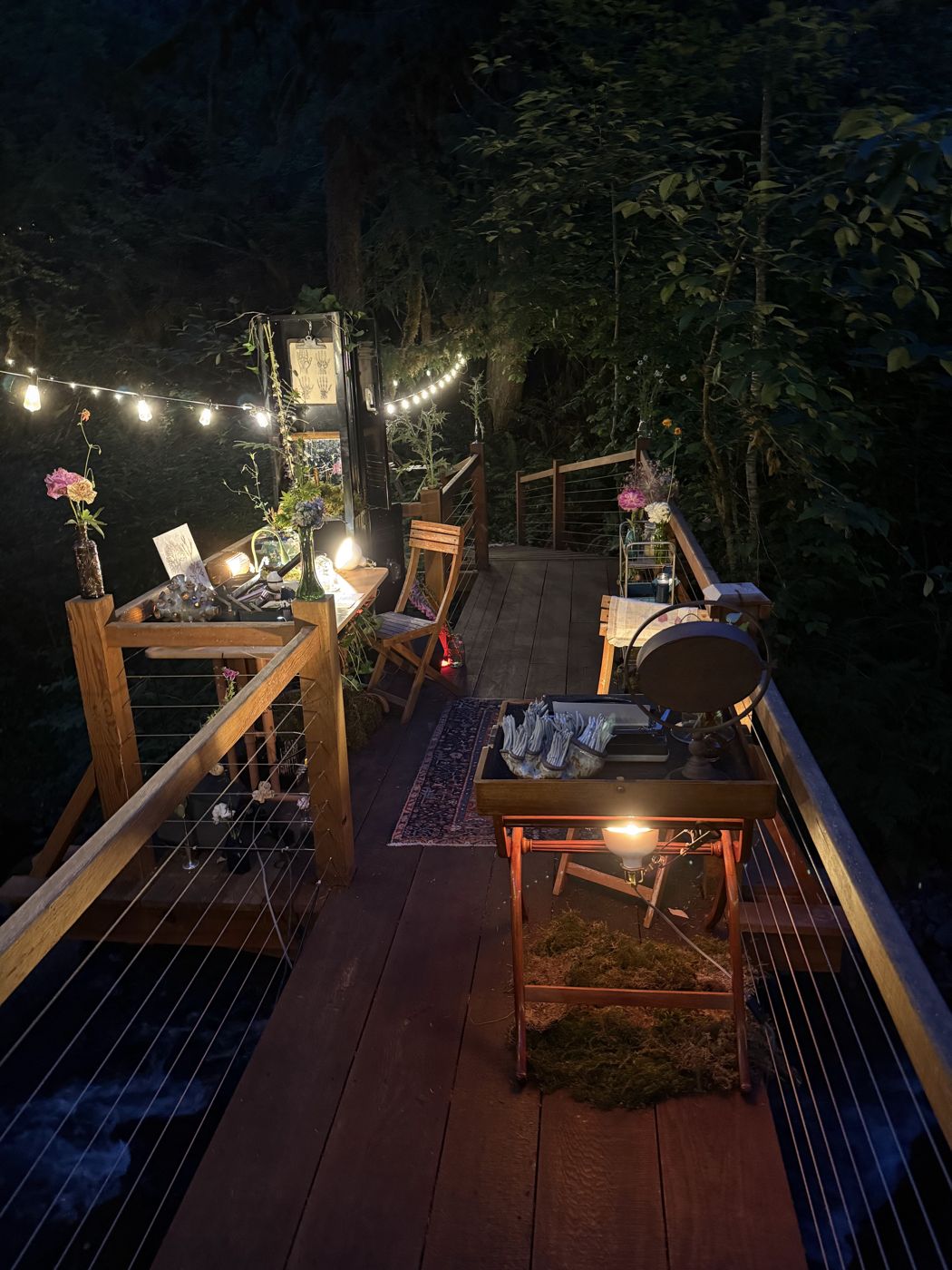 the whole scene at night: string lights over the bridge, the station glowing above the creek